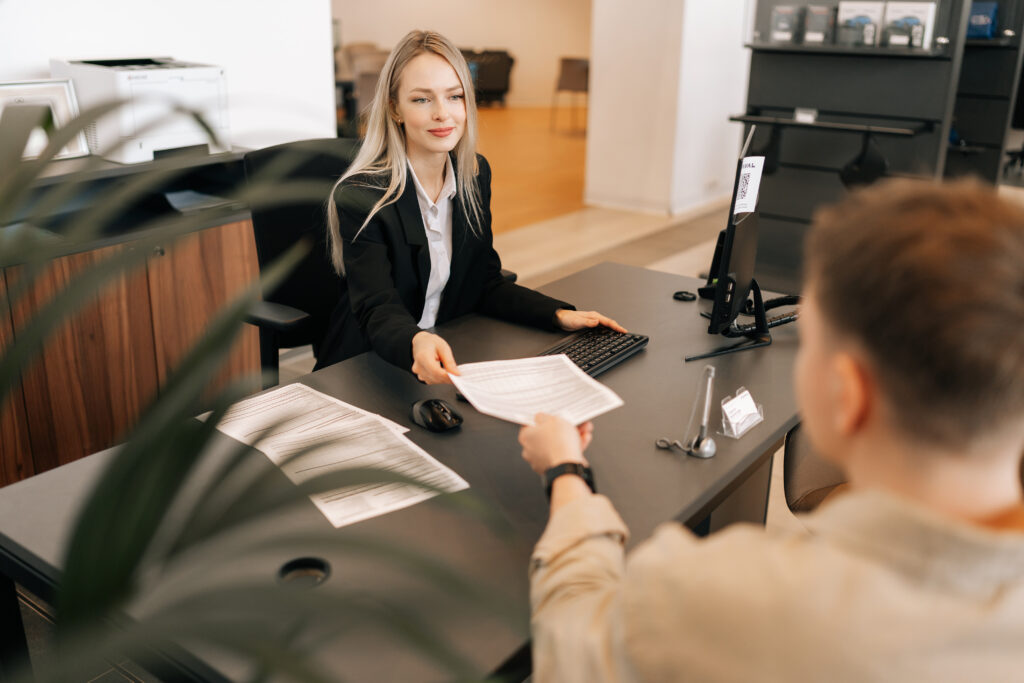 high angle back view of female manager talking about business tasks with male colleague, giving papers documents at table in office.