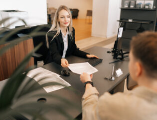 high angle back view of female manager talking about business tasks with male colleague, giving papers documents at table in office.