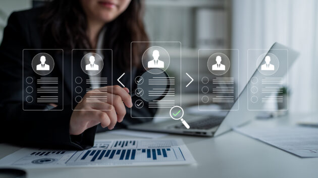 professional businesswoman reviewing resumes and analyzing data in modern office environment with graphs and charts displayed on a laptop screen. glyphic